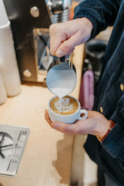 Von oben gießt anonymer Barista Milch in eine Tasse Kaffee, während er in der Cafeteria Latte Art macht — Stockfoto