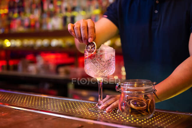 Barista irriconoscibile che decora un cocktail tonico al gin con uno scivolo di limone secco nel bar — Foto stock