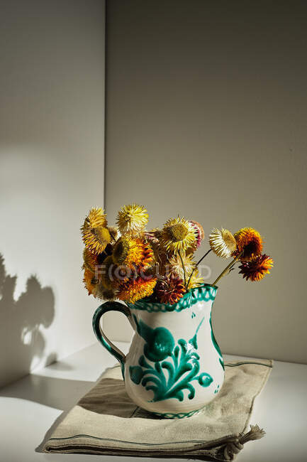 Bouquet of fresh strawflowers in ceramic pitcher placed on table in room with sunlight — Stock Photo