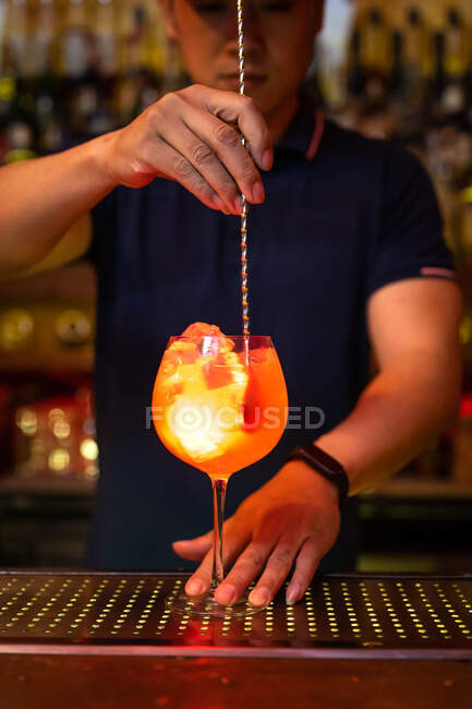 Молодой азиатский бармен держит стакан и перемешивает коктейль из грейпфрутового сока в баре — стоковое фото