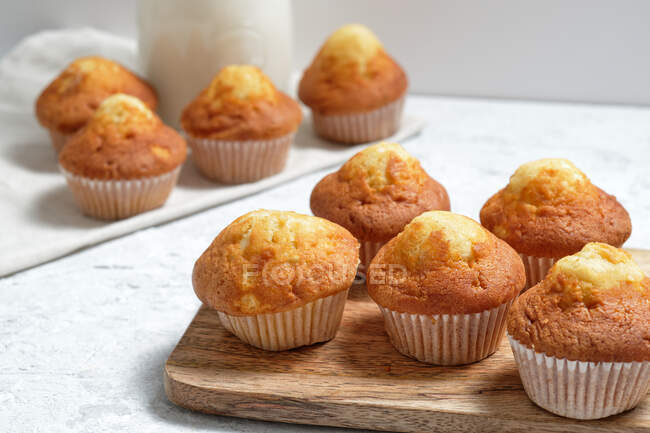 Deliziosi muffin dolci fatti in casa appena sfornati in bicchieri di carta disposti sul tavolo con barattolo di vetro di latte fresco — Foto stock