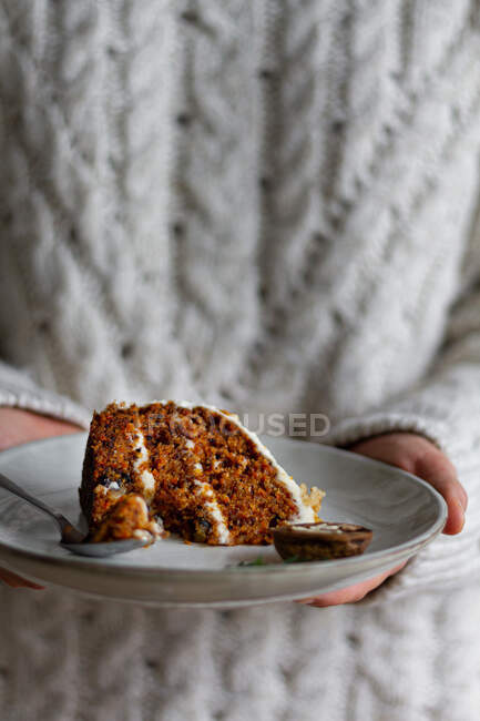 Cultive o cozinheiro anônimo segurando prato com saborosa fatia de bolo de cenoura com queijo creme e biscoito úmido — Fotografia de Stock