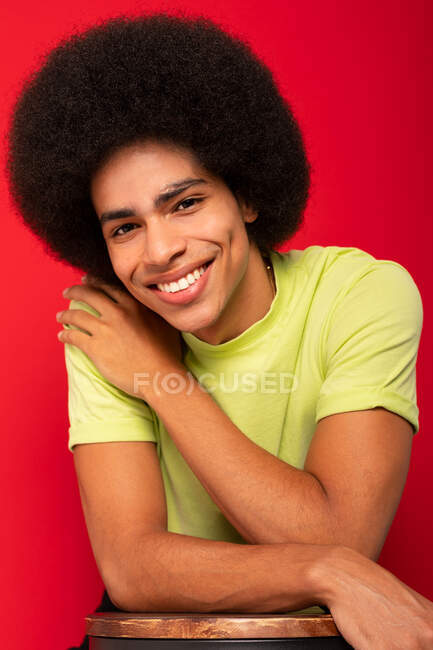 Молодой самодовольный афроамериканец в обычной футболке смотрит в камеру на красном фоне — стоковое фото