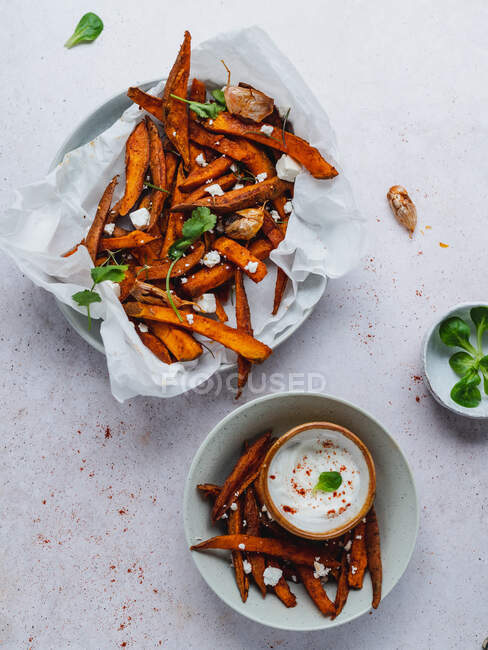 Hoher Winkel von leckeren Süßkartoffelfrites mit saurer Sahne und Kräutern auf dem Tisch serviert — Stockfoto