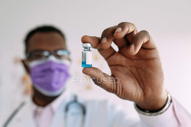 Anonymous African American male in uniform with stethoscope showing blurred vaccine in hand in hospital — Stock Photo