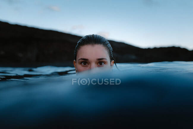 Female traveler swimming in clean blue water against rocky cliff during trip looking at camera — Stock Photo