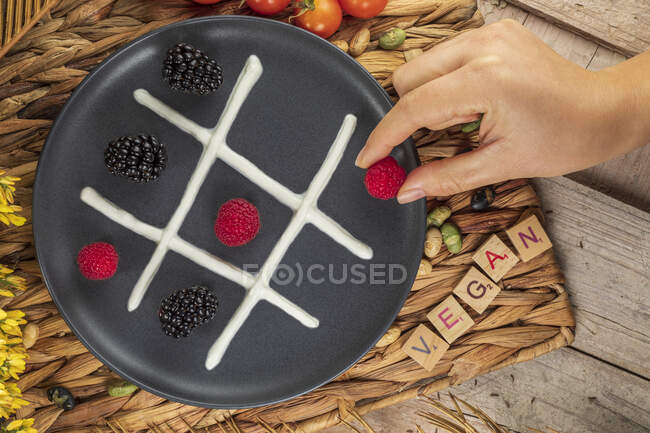 Top view of crop unrecognizable cook putting whole raspberry on plate with blackberries and whipped cream representing noughts and crosses game — Stock Photo