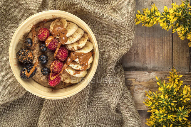 Overhead view of bowl with mix of ripe berries and banana slices covered with delicious caramel sauce on crumpled sackcloth — Stock Photo