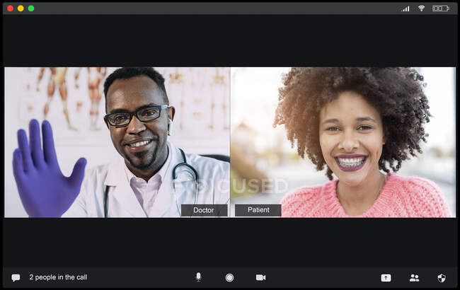 Médico masculino afro-americano positivo em uniforme médico e luvas acenando a mão e sorrindo enquanto saúda paciente feminina étnica durante videoconferência — Fotografia de Stock