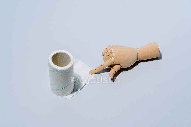 Composición de manos de madera con rollo de papel higiénico blanco sobre fondo azul - foto de stock