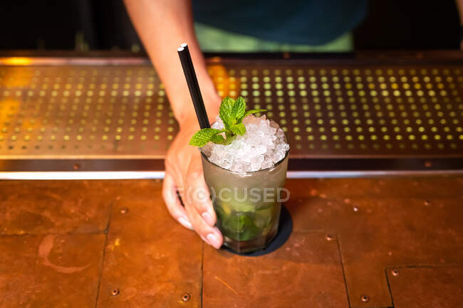 Hand of unrecognizable bartender gives you a well elaborated mojito cocktail in the bar after he finished to prepare it — Stock Photo