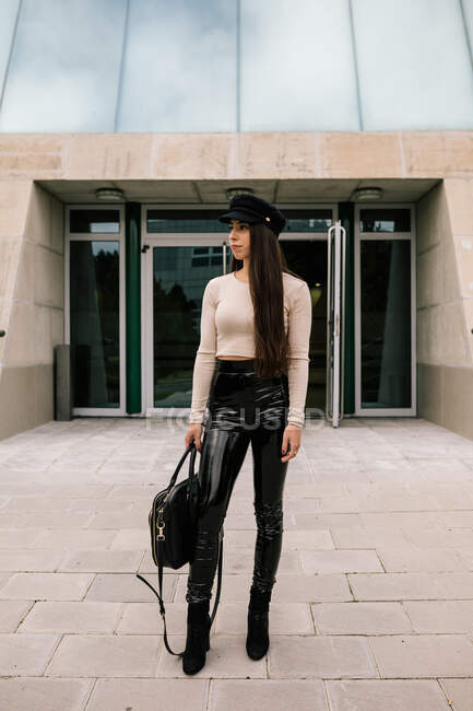 Jovem empresária na moda de pé perto da entrada do edifício contemporâneo na cidade e olhando para longe — Fotografia de Stock