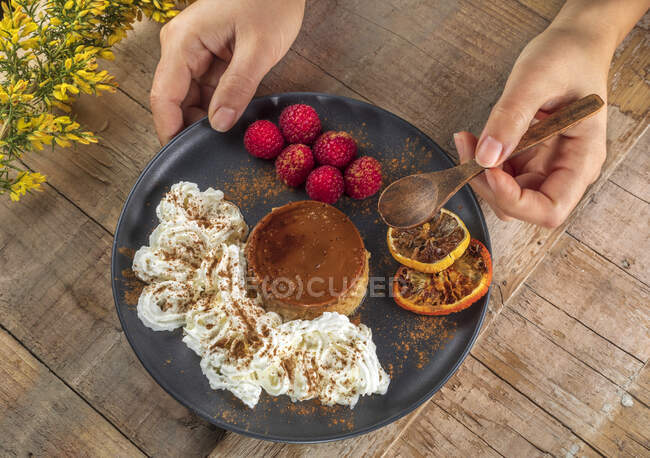 From above of crop anonymous cook with plate of yummy baked flan with ripe raspberries and cinnamon powder — Stock Photo