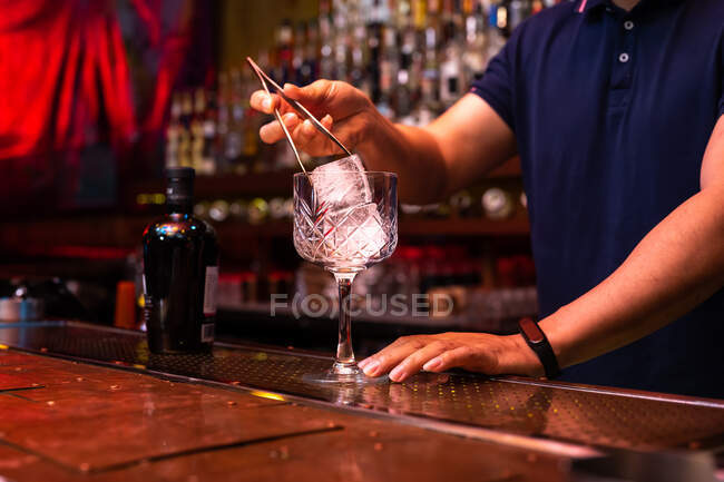 Unbekannter Barkeeper steckt einen großen Eiswürfel ins Glas, während er in der Bar einen Gin Tonic Cocktail zubereitet — Stockfoto