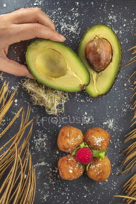 Сверху кукурузы анонимный повар со спелыми половинками авокадо рядом с аппетитными жареными крокетками с малиной сверху — стоковое фото
