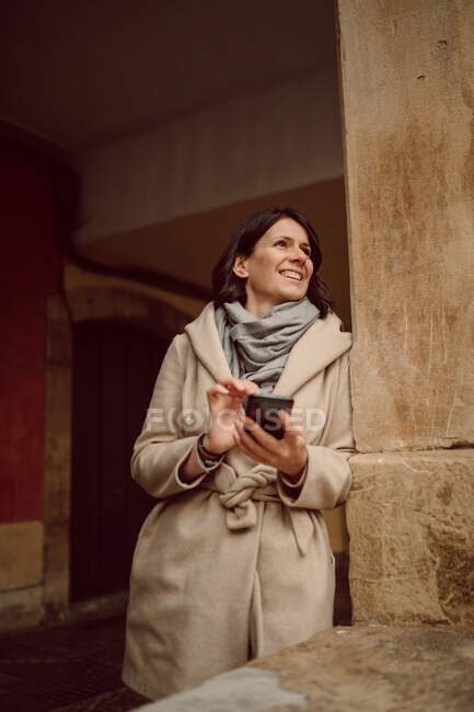 Передній погляд на стоячу жінку у зовнішньому одязі СМС-повідомлення на мобільному телефоні, поки дивишся у далечінь — стокове фото