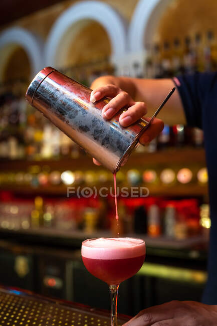 Detalle de la mano del camarero irreconocible trabajando en el bar con su agitador y vertiendo un cóctel en el vaso - foto de stock