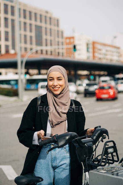 Muslim female in headscarf using bicycle sharing system in city — Stock Photo