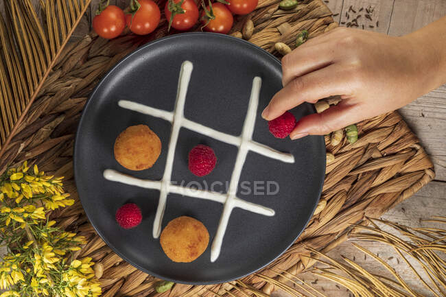 Top view of crop unrecognizable cook putting whole raspberry on plate with fritters and whipped cream representing noughts and crosses game — Stock Photo