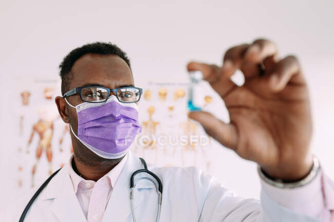 African American male in uniform with stethoscope showing blurred vaccine in hand in hospital — Stock Photo
