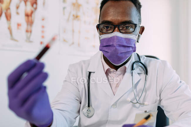 African American male doctor in medical glove demonstrating test tube with blood sample on white background — Stock Photo