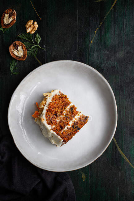 Vista superior de delicioso pastel con queso crema servido en el plato con rodajas de zanahoria fresca y nueces - foto de stock