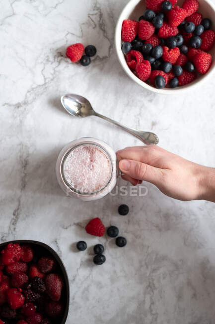 From above of unrecognizable crop person with cup of healthy smoothie with assorted berries placed on marble table — Stock Photo