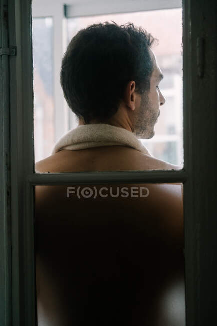 Вид сзади на мужчину с обнаженным туловищем, стоящим у окна дома и закрытыми глазами — стоковое фото