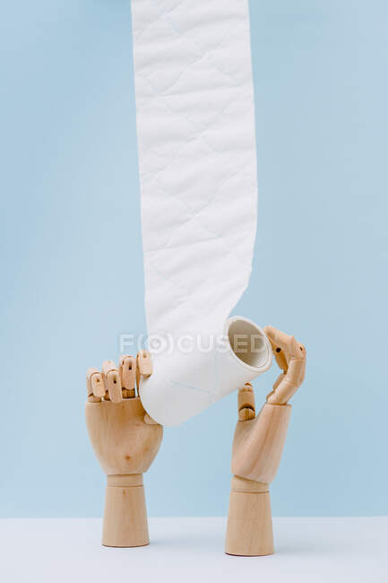 Composizione delle mani di legno svolgitura rotolo di carta igienica bianca sullo sfondo blu — Foto stock