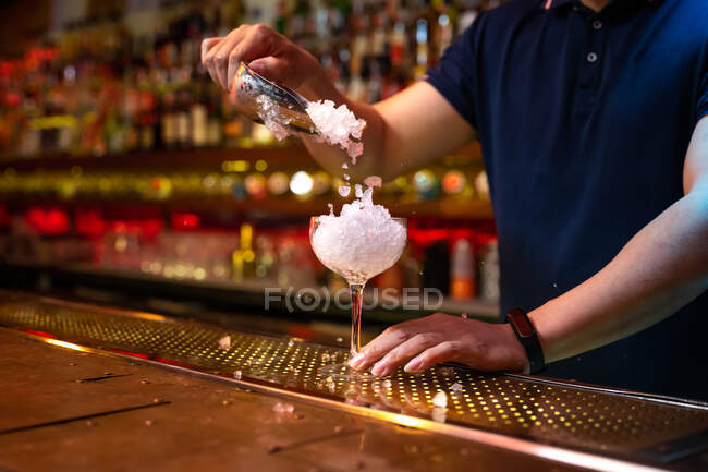 Руки неузнаваемого бармена, кладущего в чашку дробленый лёд во время приготовления коктейля в баре — стоковое фото