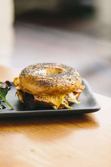 Antipasto panino al bagel con formaggio e pollo servito sul piatto con insalata di rucola sul tavolo nel caffè — Foto stock