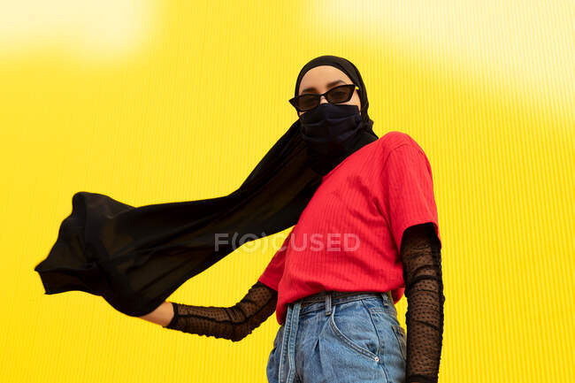 Знизу етнічної жінки в яскравому повсякденному вбранні та хустці дивиться на камеру під час пандемії COVID 19 — стокове фото