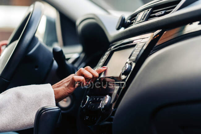 Crop anonymous female touching screen of multimedia control panel in luxury automobile in daytime — Stock Photo