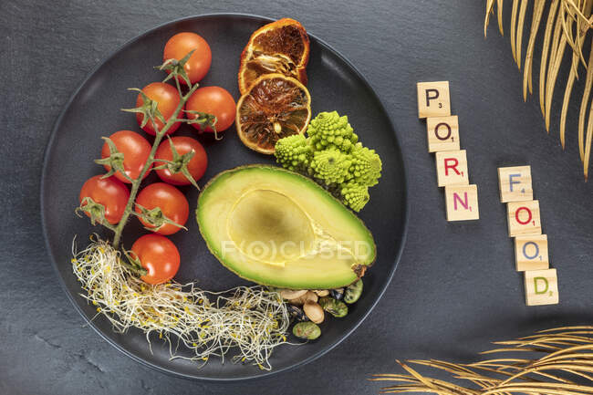 Top view of decorative inscription near plate with fresh half of avocado and bundle of cherry tomatoes near red orange slices — Stock Photo