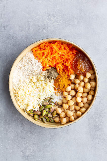 Вид сверху на миску с ингредиентами для овощного карри и манго чатни-бургера, включая горошек, морковь и сыр со специями и хлебными корочками — стоковое фото