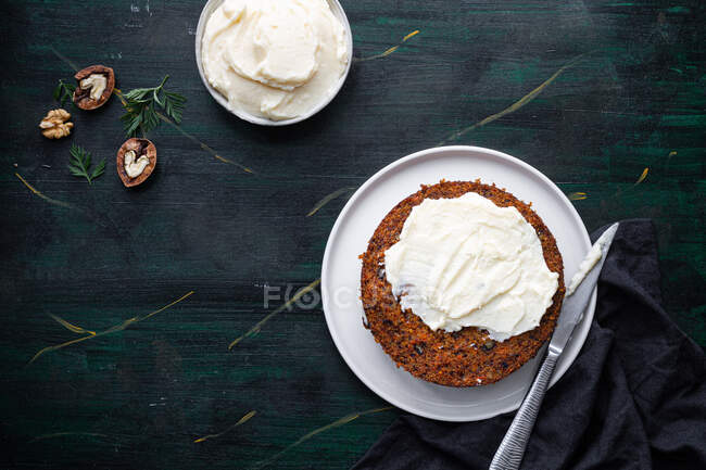 Overhead view of tasty soft cake biscuit on plate with spread cream and walnut halves on table — Stock Photo