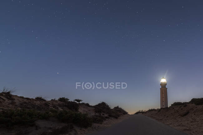 Lighthouse with bright lights placed on sandy beach in Faro de Trafalgar in Cadiz in Spain under night sky with stars — Stock Photo