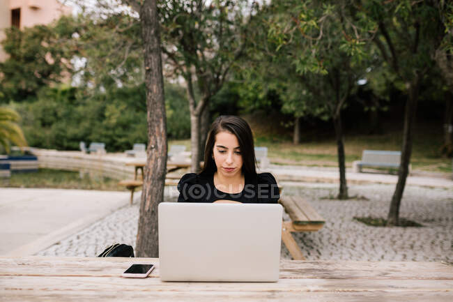 Сфокусована жінка-підприємець сидить за столом з ноутбуком в парку, працює віддалено — стокове фото