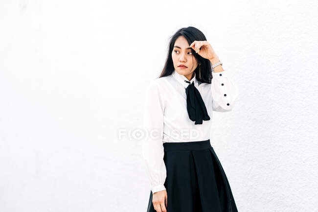 Серйозна етнічна жінка в уніформі стоїть на білому тлі і дивиться на камеру — стокове фото