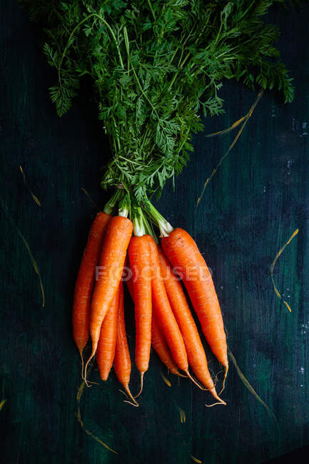 Vista superior de racimo de zanahorias crudas enteras con tallos y hojas en superficie de madera - foto de stock