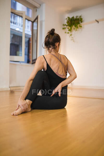 Back view of anonymous barefoot female in sports clothes stretching leg while practicing yoga on parquet — Stock Photo