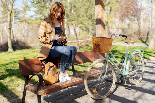 Junge Frau schreibt SMS auf Handy in der Nähe von Fahrrad mit hölzernem Weidenkorb — Stockfoto