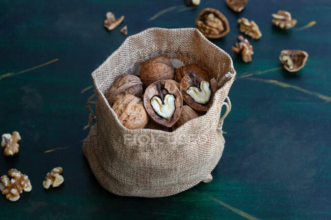De arriba bolsa con nueces enteras y cortadas a la mitad con nueces secas y centro en forma de corazón en la mesa - foto de stock