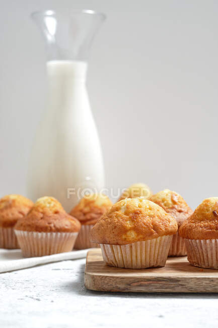 Delicioso caseiro recém-assado muffins doces em copos de papel dispostos na mesa com frasco de vidro de leite fresco — Fotografia de Stock