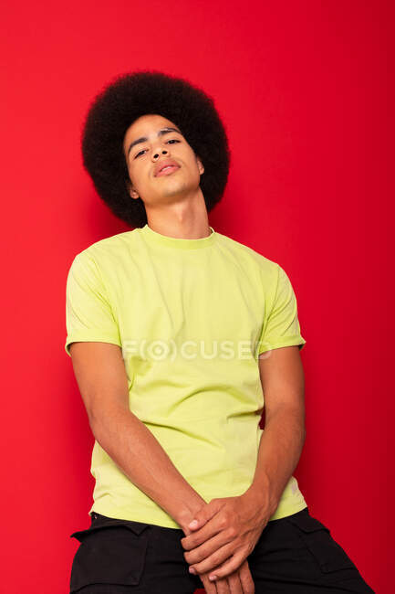 Joven hombre afroamericano seguro de sí mismo en camiseta casual mirando a la cámara en el fondo rojo - foto de stock