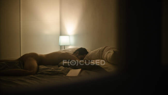 Вид збоку оголеного чоловіка лежить на м'якому ліжку і спить у затишній спальні з тьмяним світлом — стокове фото