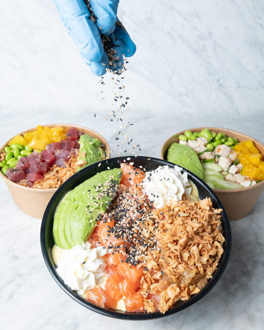 Crop unrecognizable chef decorating bowl with tasty poke dish served on marble table — Stock Photo
