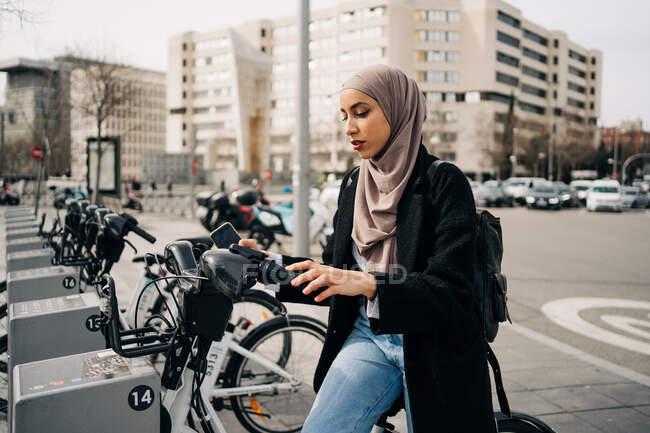 Seitenansicht einer Muslimin mit Kopftuch beim Fahrradverleih in der Stadt — Stockfoto