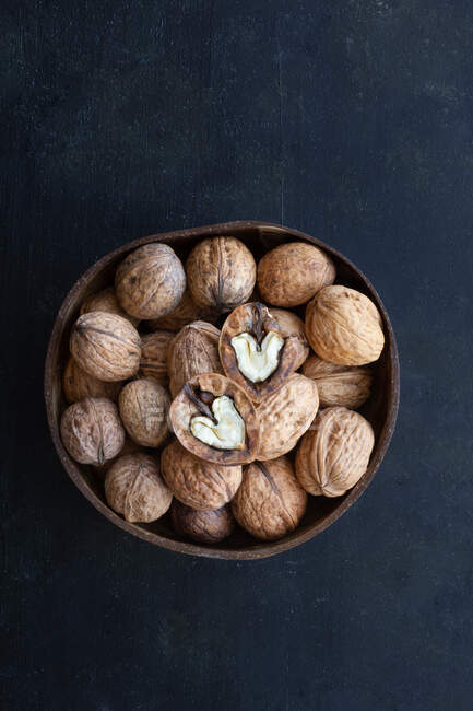 Round shaped wooden bowl full of crunchy walnuts with dry uneven nutshells on table — Stock Photo