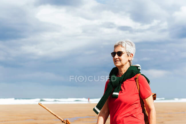 Senior female trekker walking on sandy shore against endless sea during trip — Stock Photo